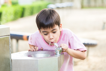 Little boy drinking water in the public parkの写真素材