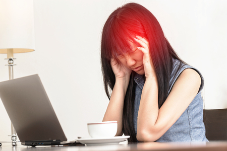 Asian Woman having a headache while she works on a laptopの写真素材