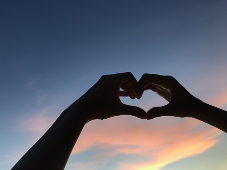 man hands make heart shape symbol up into amazing dark blue and orange sky, valentine's day conceptの写真素材