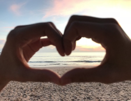man hands make heart shape symbol at beautiful beach when sunrise, selective focus, valentine's day conceptの写真素材