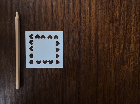 natural brown wood pencil and white square blank paper which was punched in heart shape on dark brown wood table with copy space on right side of frame, "valentine's dayâ conceptの写真素材