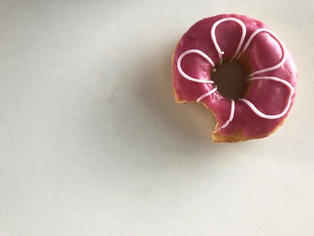 flower-like pink doughnut which was bit on white background in day light with copy space on left...