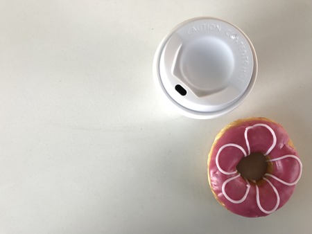 top view shot of white cup of hot coffee and flower-like pink doughnut on white background in studio with copy space on left side of frameの写真素材