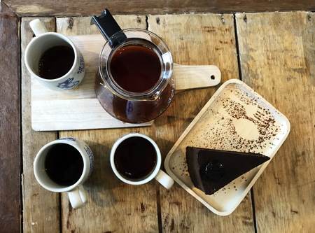 top view shot of three cups of drip coffee, coffee jar and piece of chocolate cake on natural brown wood tableの写真素材