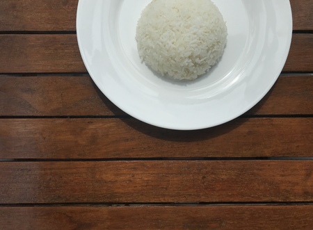 cropped shot of plain Thai rice on white plate put on brown wooden table with copy space at the bottom of frameの写真素材