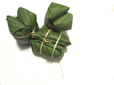 raw thai traditional dessert which called khao tom mud in thai or bananas with sticky rice which are wrapped with green banana leaf and flat thin bamboo strip on white backgroundの写真素材