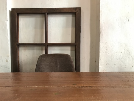 empty wooden table top, brown chair and antique wooden window frame with white cement wall in coffee...