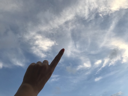 woman use her left index finger pointing up in the bright blue sky with white cloud in daylight with copy space on the right side of frameの写真素材