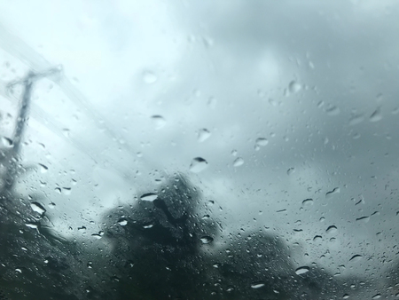 rain drops on car's windscreen with blurred stormy sky, electric pole and trees along the road on...
