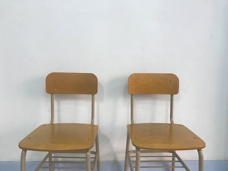 two brown empty school chairs with white wall on background in natural daylightの写真素材