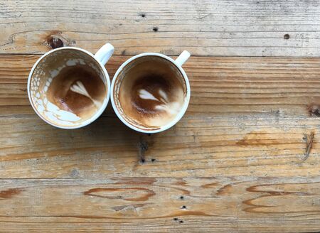 two finished cups of hot latte coffee with leftover latte art, put on natural brown and grunge pattern wood table with copy space at right side of frameの写真素材