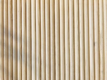 full frame shot of natural light brown rubber softwood logs attached together as a wall with a little leaf's shadow on the left sideの写真素材