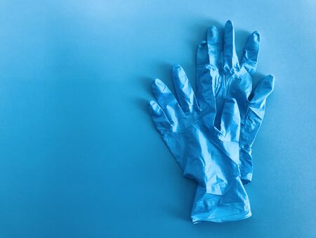 one pair of blue medical gloves which are stacking up each other on plain empty blue background with...