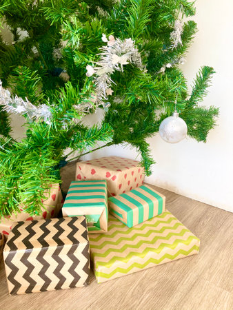many lovely colorful gift boxes are put under the green decorated Christmas tree with silver ornament and stuff on it with white wall on background and light brown wood floorの写真素材