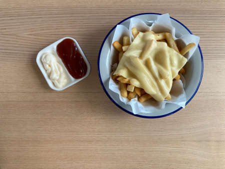 french fries with melted cheddar cheese, served with mayonnaise and ketchup, put on natural brown wood tableの写真素材