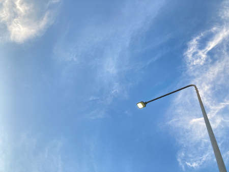 turn-on street metal lamp post under the clear blue sky and light white clouds with copy space on the left side of the frameの写真素材