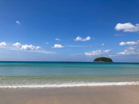 fisherman's boat in the deep blue sea with a green hill, blue sky, white cotton clouds, and sea waves on the beachの写真素材