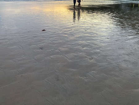A loving couple is holding hands and strolling on the beach with a scene of the twilight sunset sky and silver sea wavesの写真素材