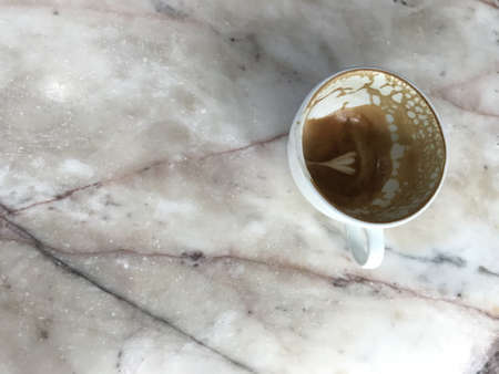 leftover tulip pattern latte art in a ceramic white coffee cup put on a white marble tableの写真素材