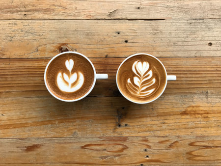 tulip and rosetta pattern latte art of two cups of hot latte coffee put in the middle of natural brown and beautiful pattern wood tableの写真素材