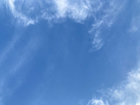 the little crescent moon on the upper right corner of the bright blue sky with white clouds in natural daylightの写真素材