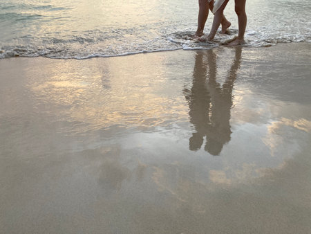the legs of a strolling couple on the sunset beach with vanilla sky shining on the clear sand