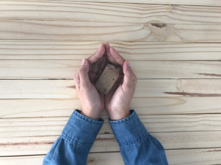 a woman in blue jeans shirt is holding a small brown ceramic house with her both hands on natural light brown rubber tableの写真素材