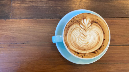 blue cup of hot cappuccino coffee with gorgeous lily flower latte art on dark brown wooden table from top view shotの写真素材
