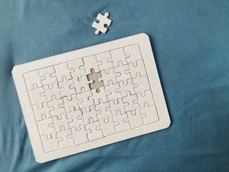 almost finished all-white jigsaw puzzles with the last piece on the green-blue cotton fabric backgroundの写真素材