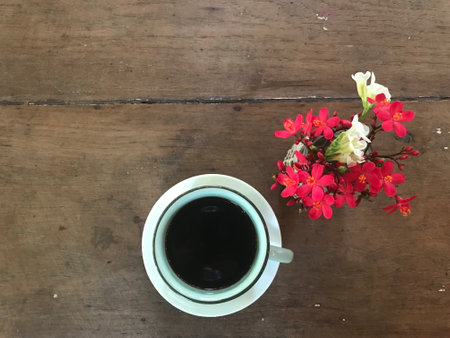cup of hot black coffee with red and white flowers, putting on an antique wooden tableの写真素材