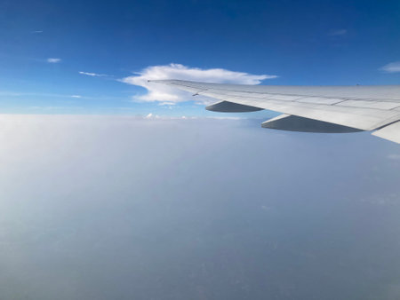 view of white cloud around the tip of the airplane's left wing and the gray smoke covering the town below from an airplane window when up in the skyの写真素材