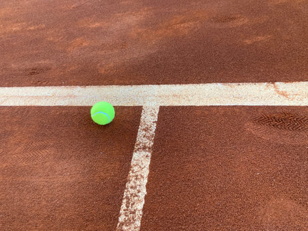 the bright green tennis ball lands exactly on the center line of the red clay courtの写真素材