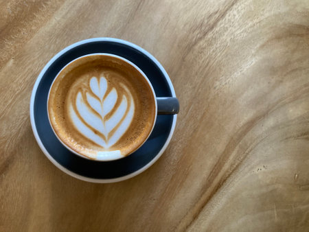hot cappuccino coffee with gorgeous lily flower latte art in dark blue cup on natural wood table with beautiful wood grain with copy space on the right side of frameの写真素材