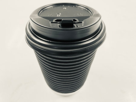 close up shot of black paper cup of black coffee with a black plastic lid for take-away is placed in the middle of a bright white tableの写真素材