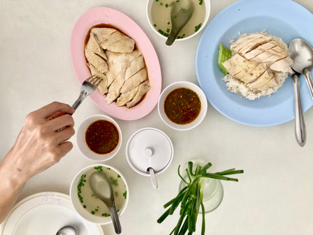 A woman is scooping a plate of Betong chicken, sliced and paired with steamed rice, with special sauce and green onions, accompanied by a chicken bone soup on a white tableの写真素材