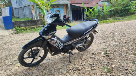 Rear view of a black motorbike parked on a dirt road.の写真素材