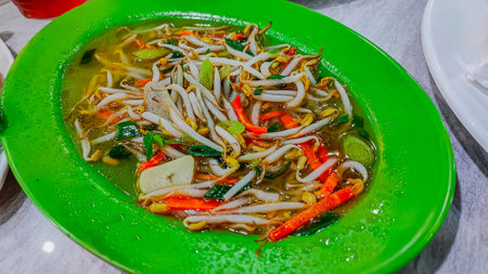 Thai noodle soup with vegetables in green plate on table.の写真素材
