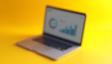Blurred Laptop Displaying Business Charts on Yellow Backgroundの素材