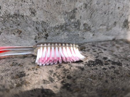 A worn toothbrush with pink and white bristles lies on a rough, textured concrete surface, showing signs of age and use.の写真素材