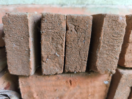A close-up shot highlights the rugged, sandy texture of stacked red terracotta bricks. These earthy building materials are commonly used in construction.の写真素材