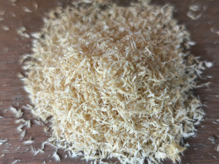 A close-up shot of a small mound of dry, light-colored wood shavings resting on a natural brown wooden surface. The texture is prominent, suggesting use for crafts or animal bedding.の写真素材