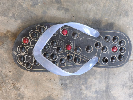 A single acupressure reflexology sandal with various massage nodes rests on a textured concrete surface, showing labeled reflex points.の写真素材