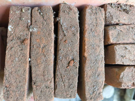 A detailed view of rough, reddish-brown clay bricks stacked, showing aged texture, dust, and small debris. Gaps between the bricks reveal their weathered condition.の写真素材