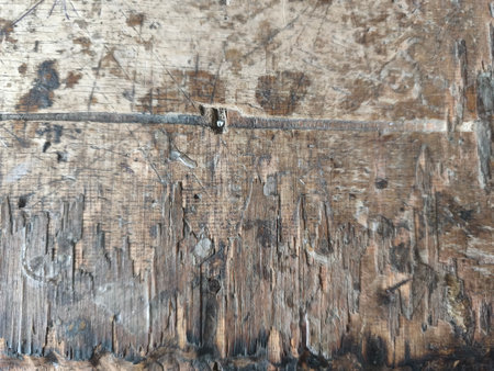 A detailed close-up shows the surface of an old, weathered wooden board. It features deep scratches, dark stains, and splintered sections, highlighting its rough and aged texture.の写真素材