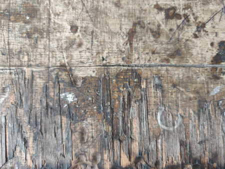 A detailed close-up reveals the rough texture of a weathered wooden surface, featuring prominent scratches, deep grains, and dark stains. This aged plank evokes a rustic and durable aesthetic.の写真素材