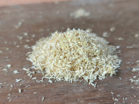 A close-up shot of a small pile of light-colored wood shavings resting on a brown wooden surface. Small fragments are scattered around.の写真素材