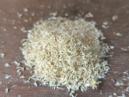 A pile of light-colored wood shavings, possibly sawdust, rests on a textured wooden surface. The fine, fluffy material forms an interesting abstract pattern against the blurred background.の写真素材