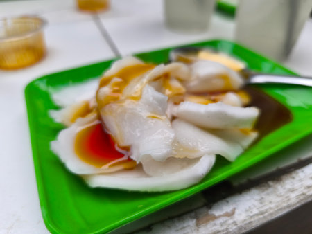 A close-up view of delicate steamed rice rolls, drizzled with sweet caramel and reddish fruit sauces, served on a vibrant green plate.の写真素材