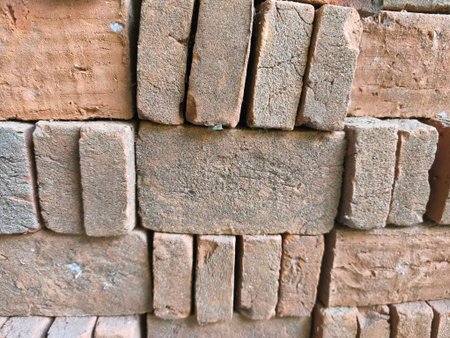 A close-up shot of stacked rustic red clay bricks, revealing their rough, granular texture and...