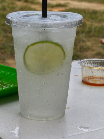 A cold, refreshing lime drink in a plastic cup with a visible lime slice and heavy condensation, resting on a white table.の写真素材